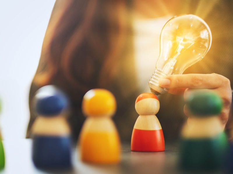 Closeup image of a woman holding and putting a light bulb over o Closeup image of a woman holding and putting a light bulb over one of a different colors wooden people toy for business concept