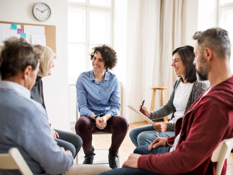 Men and women sitting in a circle during group therapy, talking.