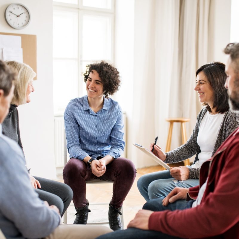 Men and women sitting in a circle during group therapy, talking.