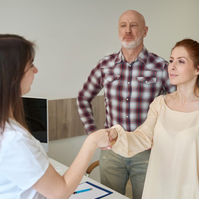 Partners shaking hands with female gynecologist in clinic
